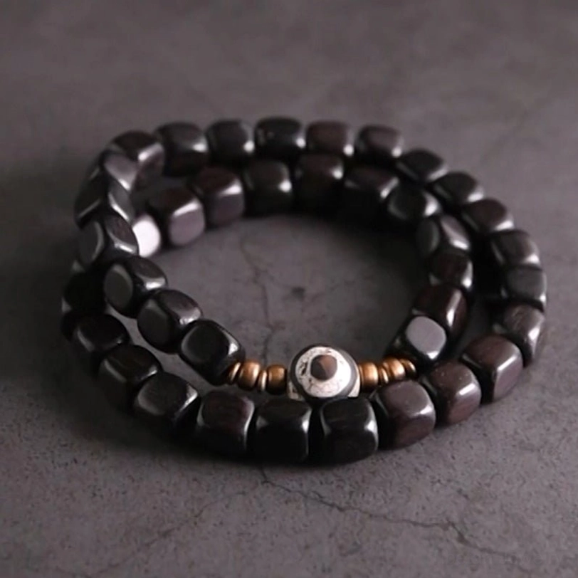 Ebony wood nine-eye dzi bead couple bracelet with copper accents, top-down flat lay view on dark cracked stone