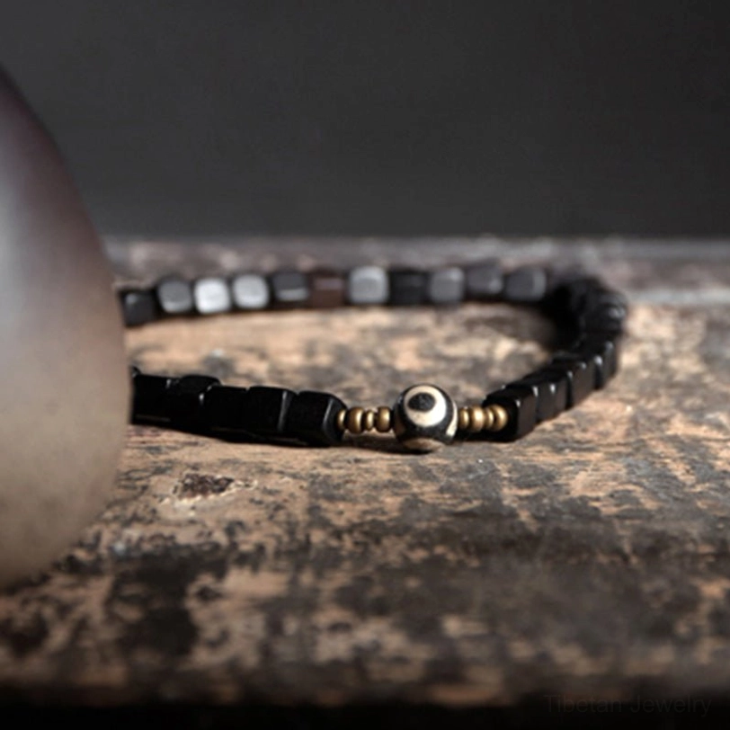 Double-strand ebony wood dzi bead couple bracelet flat lay featuring black square beads, copper spacers, and central nine-eye dzi bead on weathered wood table