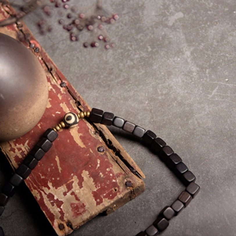 Two-piece ebony wood dzi bead couple bracelet set featuring black square beads with copper spacers and central eye dzi bead on rustic wooden prop