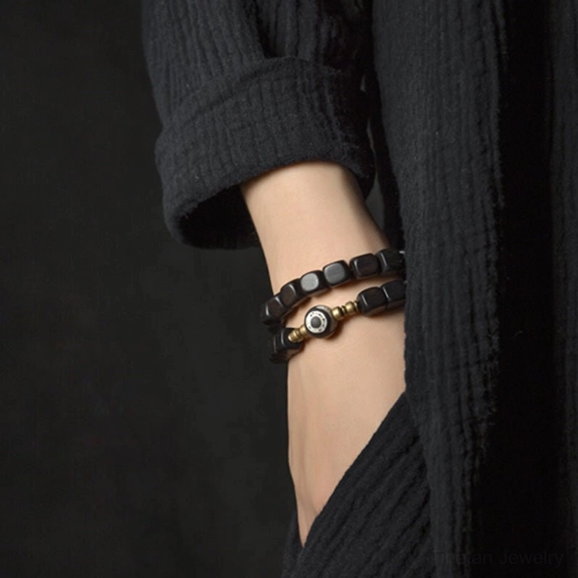 Stackable ebony wood nine-eye dzi bead couple bracelets worn on wrist, close-up view showing dark wood bead detail and eye charm against linen clothing
