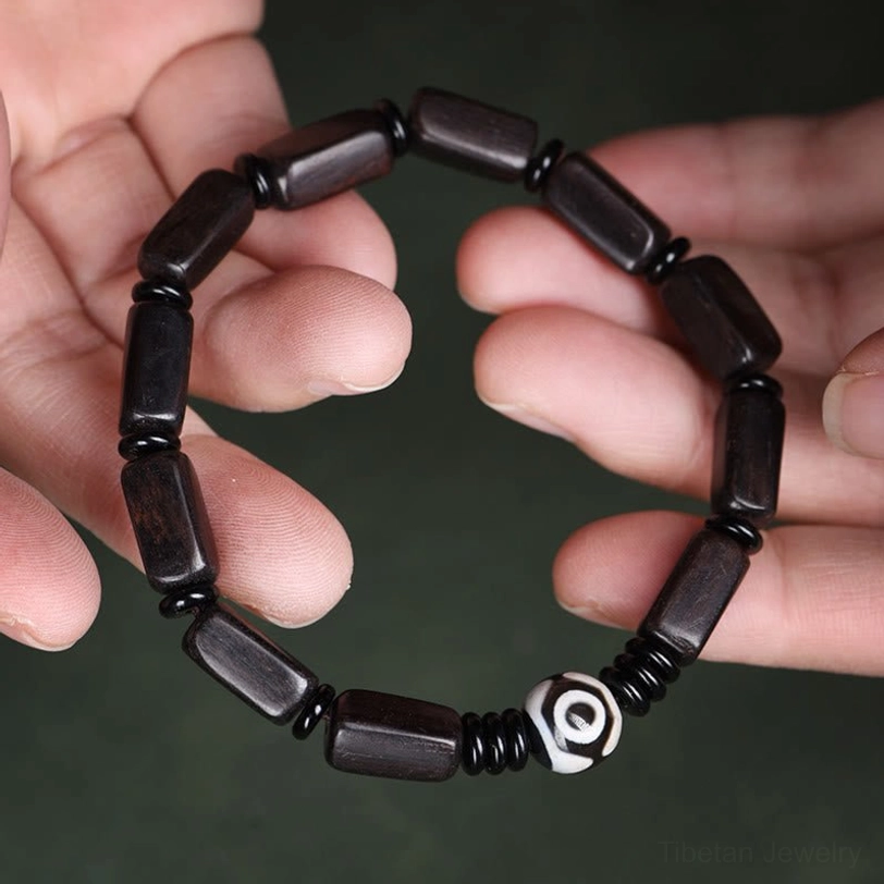 Hand-held first-person view of Tibetan ebony wood and Dzi bead balance bracelet being worn on wrist
