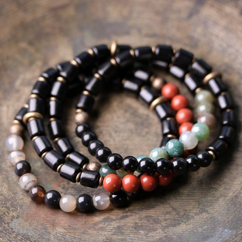 Stacked collection of multiple ebony and gemstone healing crystal bracelets displayed on wooden table showing different stone variations