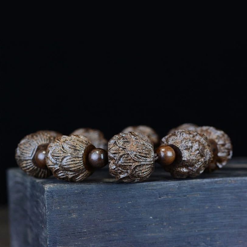 Multiple ebony wood lotus carved bracelets arranged on dark wooden surface with black backdrop