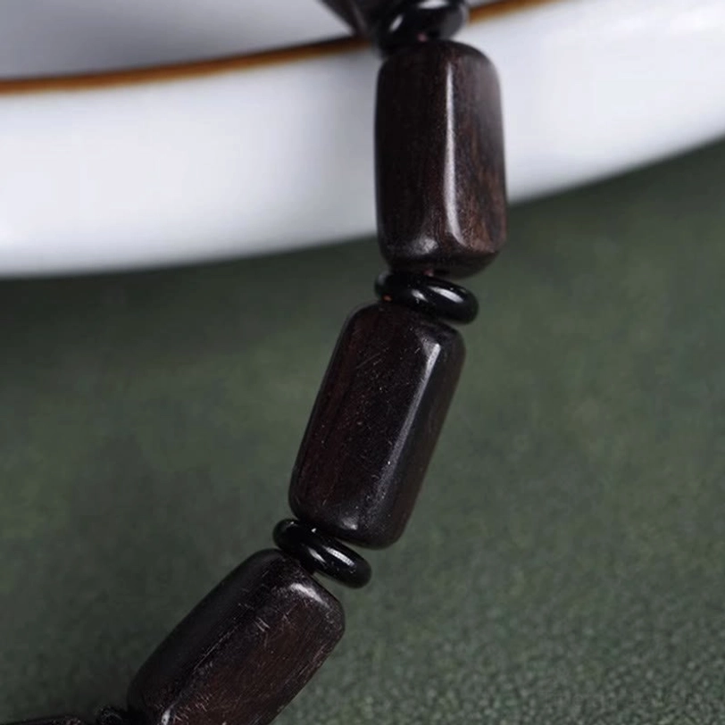 Low-angle close-up of polished rectangular ebony beads and black metal spacer rings showing bead quality