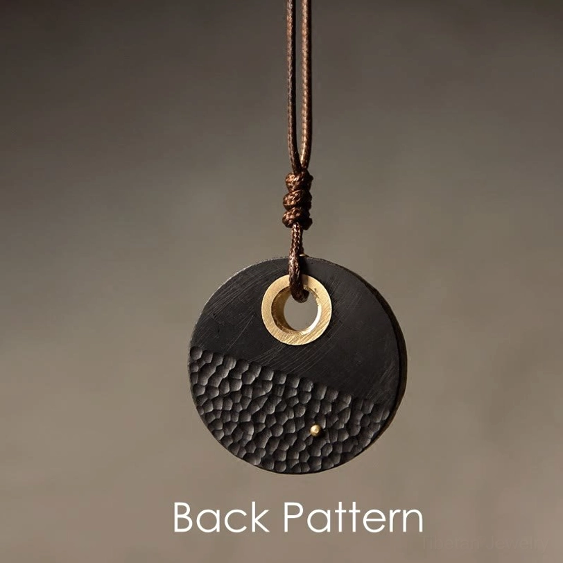 Back side of round ebony wood pendant showing brass dot detail and hammered surface