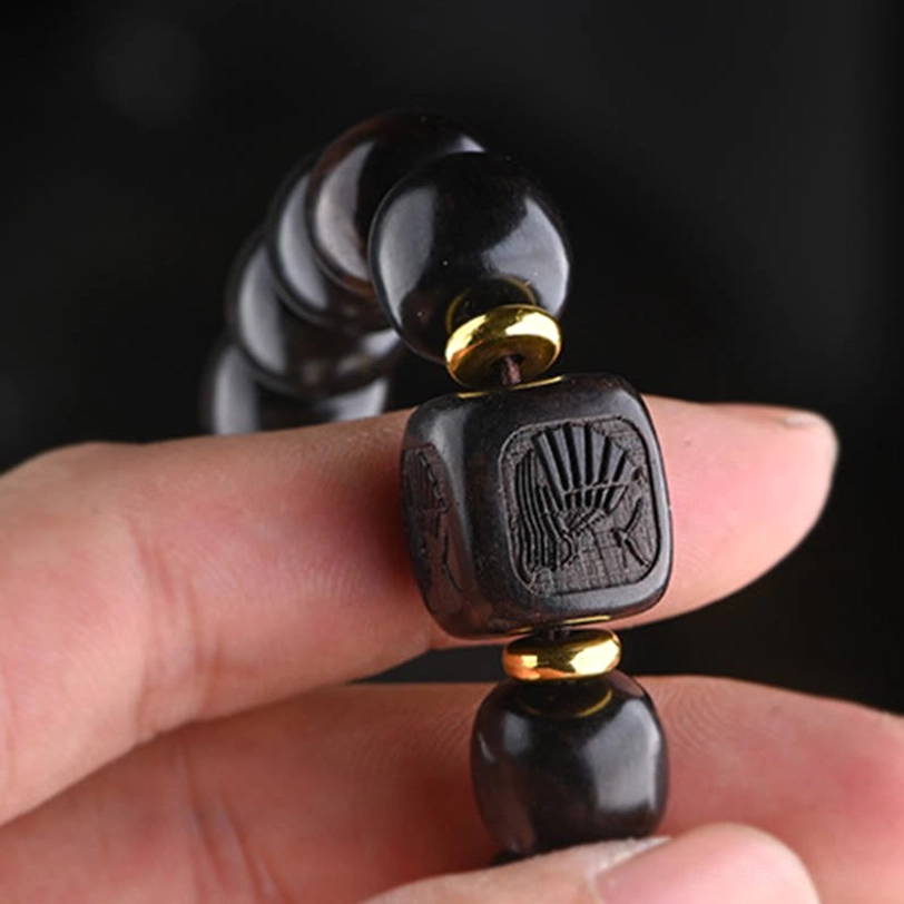 Close-up detail of carved square ebony wood bead with brass spacer and barrel-shaped wooden beads