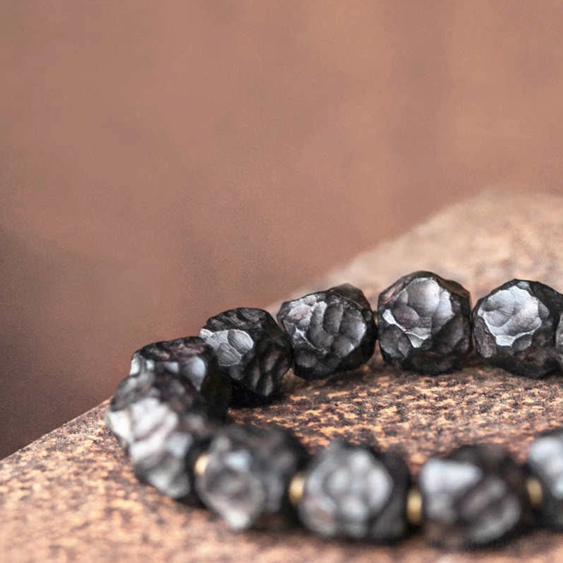 Low-angle close-up of large irregular ebony wood beads with rough matte surface and copper accent