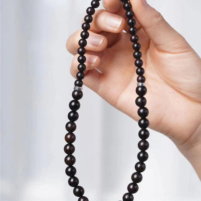 Close-up finger holding tibetan ebony wood beaded strand, detailed view of uniform dark round wooden beads with silver spacers