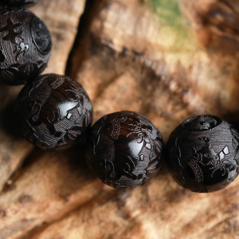 Macro close-up of hand-carved ebony wood beads showing intricate pattern details and natural grain of premium wood