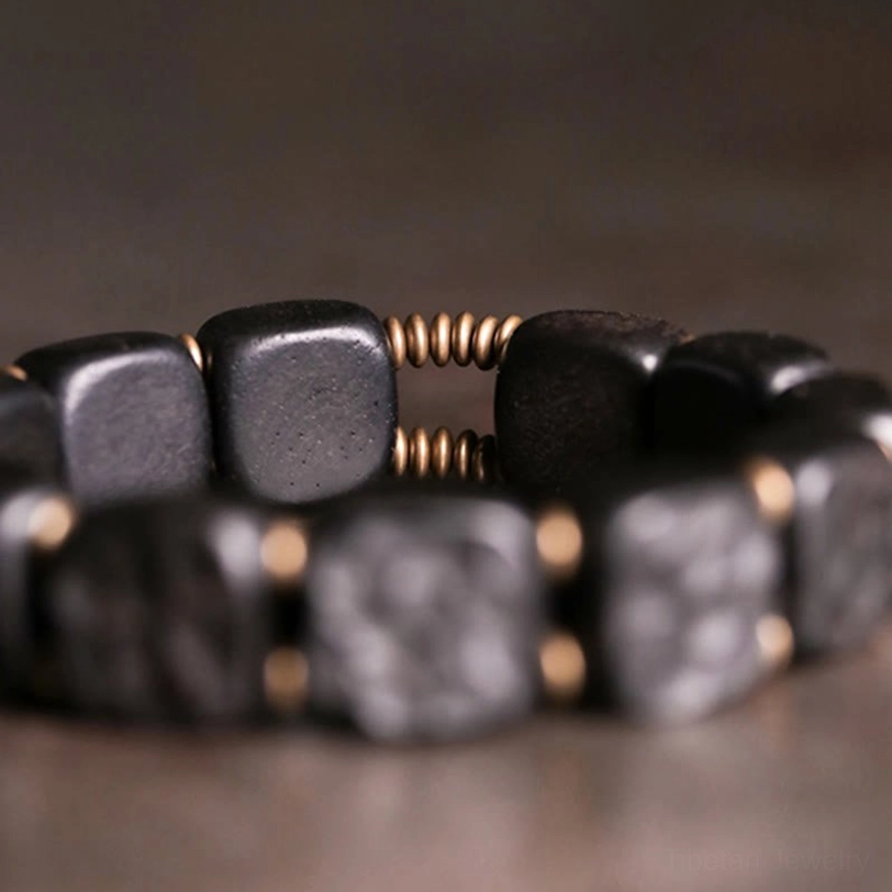 Close-up side view of bracelet showing rough chiseled ebony surface and bronze gold spring spacers between beads