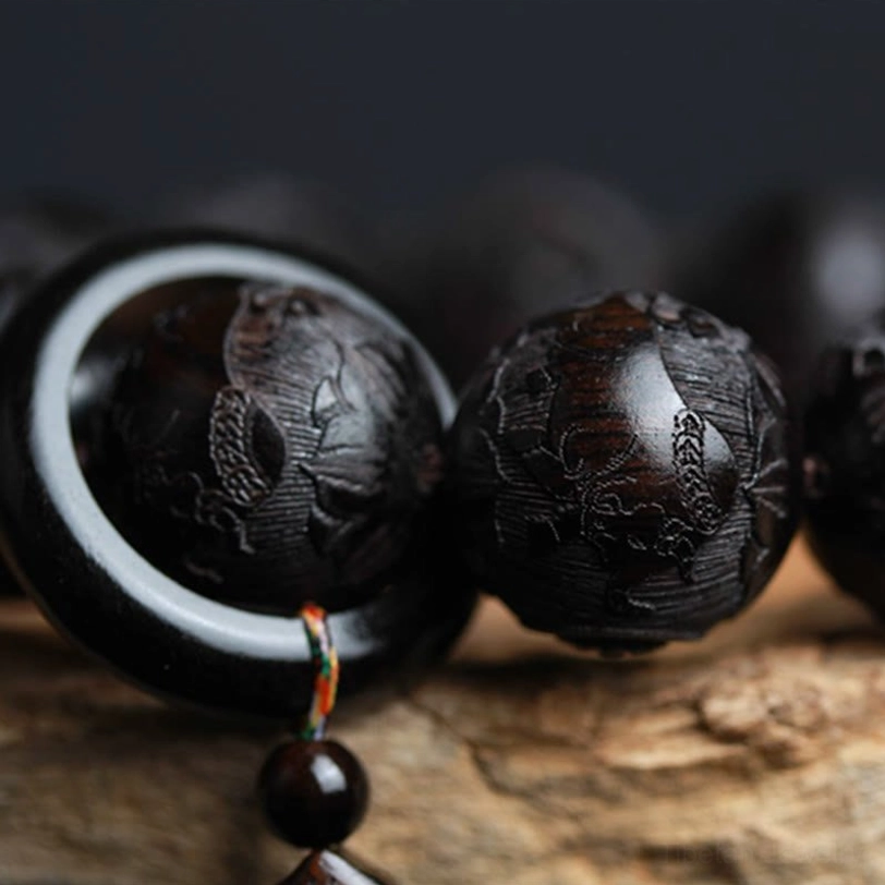 Close-up of ebony wood beads with copper ring and colorful elastic string tassels on dark blurred background