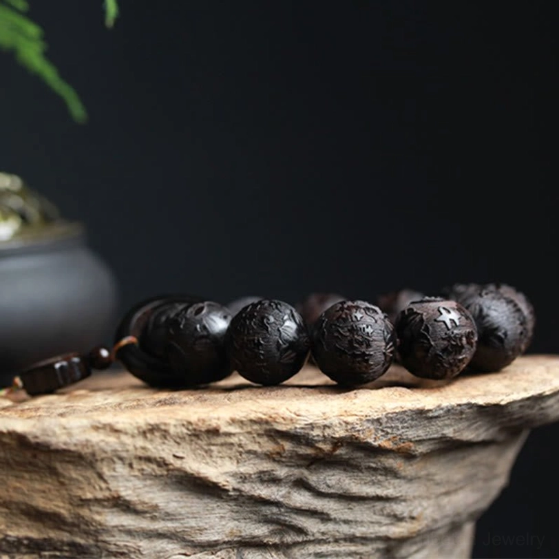 Ebony wood beaded bracelet with dark brown carved beads and small end charm lying flat on stone-textured surface