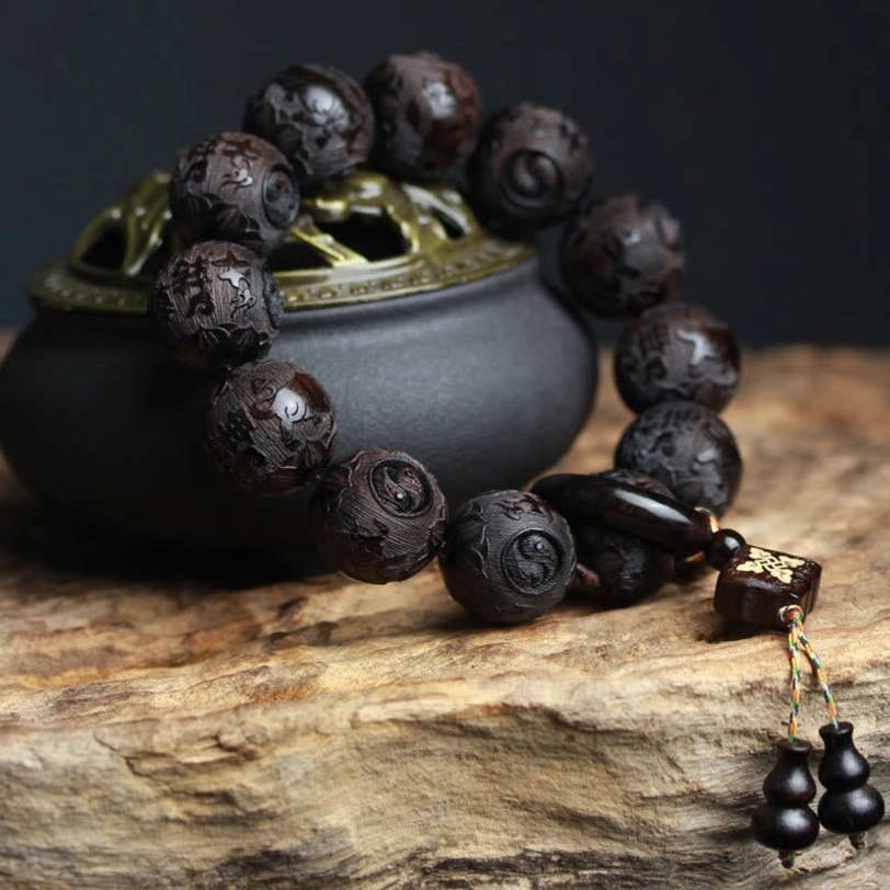 Handcrafted ebony wood balance bracelet with carved beads and gourd pendant charm displayed on vintage incense burner and wooden slab