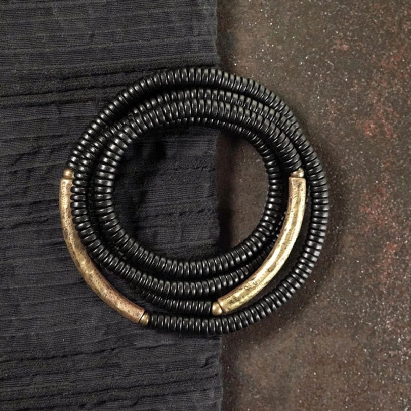 Dual-coil ebony wood brass bracelet flat lay rustic fabric background