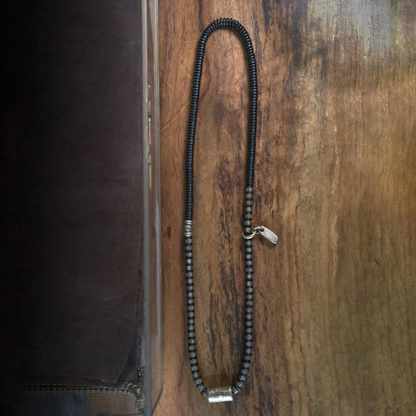 Long strand of coiled ebony wood beads with copper hardware on dark fabric background