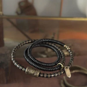 Close-up of ebony wood beads with antique copper accents on glass surface