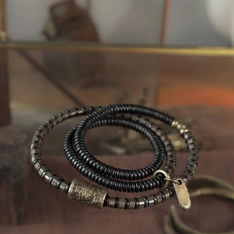 Close-up of ebony wood beads with antique copper accents on glass surface