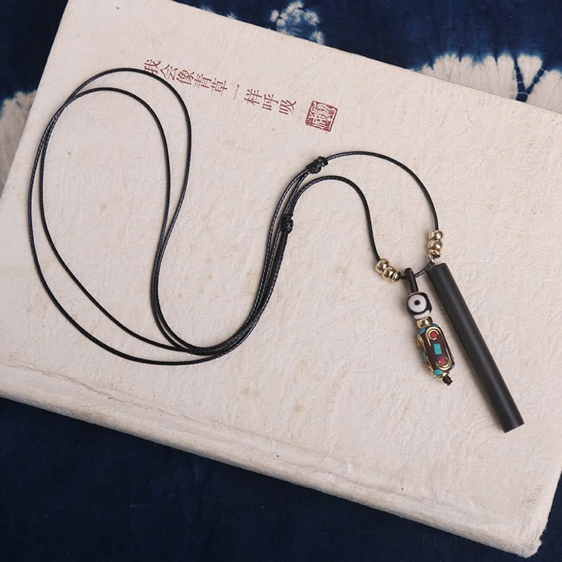 Cylindrical dark ebony wood dzi bead pendant with detailed charm close-up on textured fabric