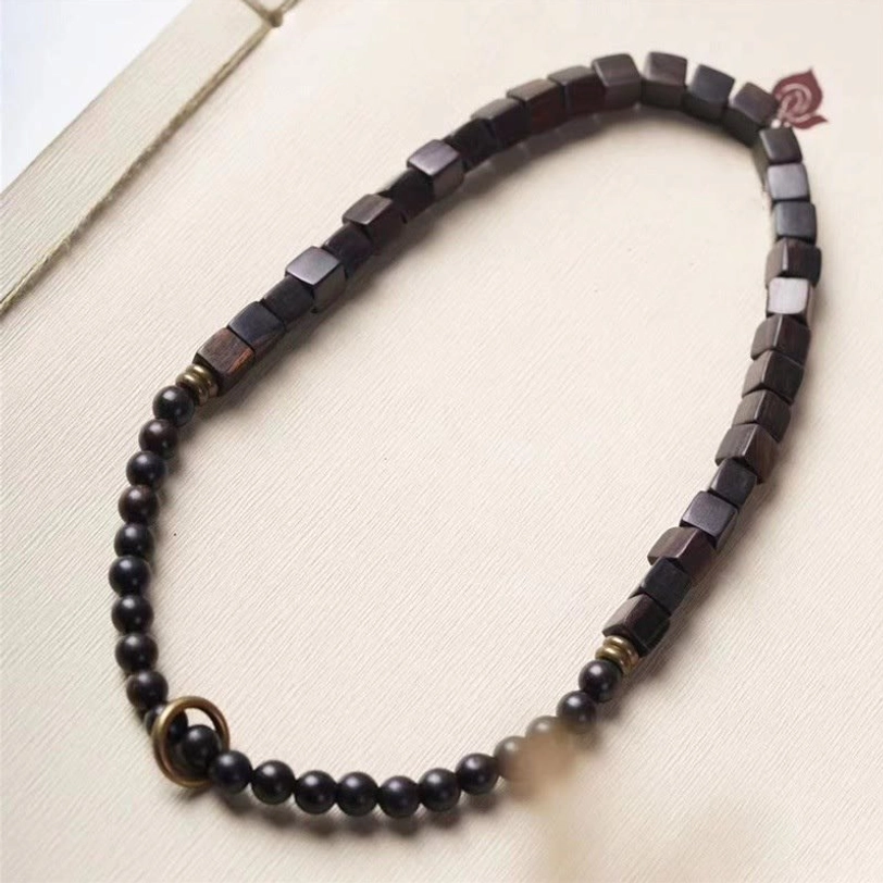 Top view flat lay of dark ebony wood double wrap bracelet on paper showing symmetrical bead arrangement and metal hardware