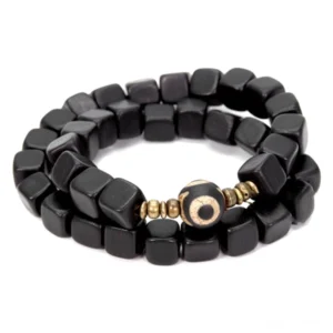 Double-strand ebony wood dzi bead couple bracelet featuring matte black cube beads with central eye charm and gold metal spacers on white studio background