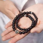 Tibetan ebony wood dzi bead double wrap bracelet held in palm, showing dark wooden beads with silver spacers and nine-eye dzi bead detail
