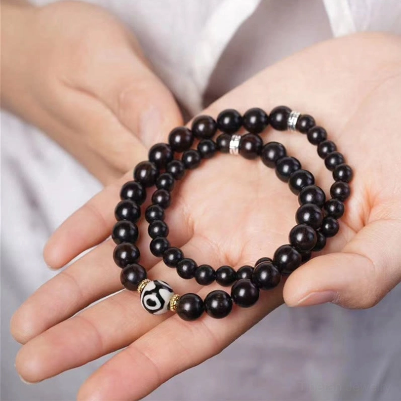 Tibetan ebony wood dzi bead double wrap bracelet held in palm, showing dark wooden beads with silver spacers and nine-eye dzi bead detail