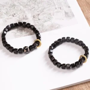 Pair of matching ebony wood dzi bead bracelets displayed on white paper with wooden table background