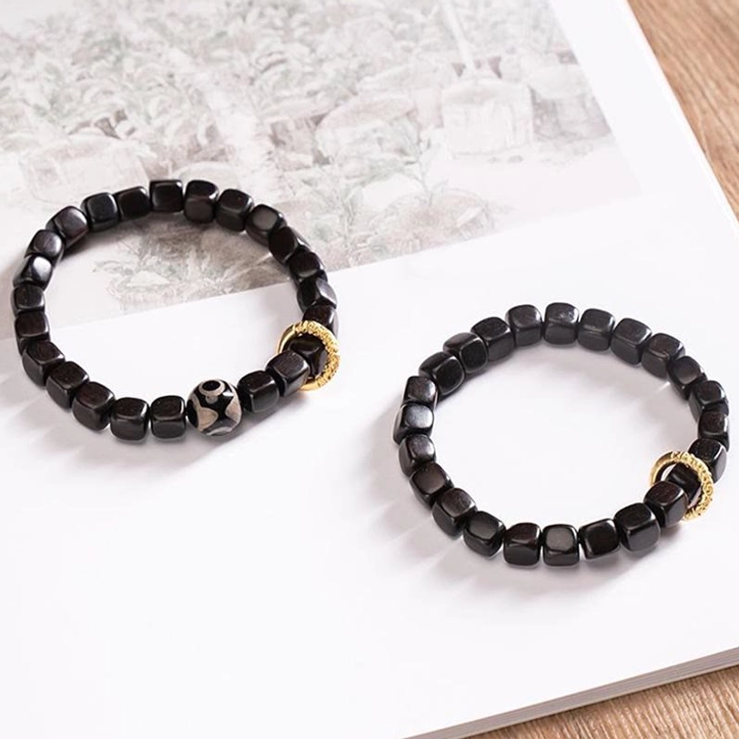 Pair of matching ebony wood dzi bead bracelets displayed on white paper with wooden table background