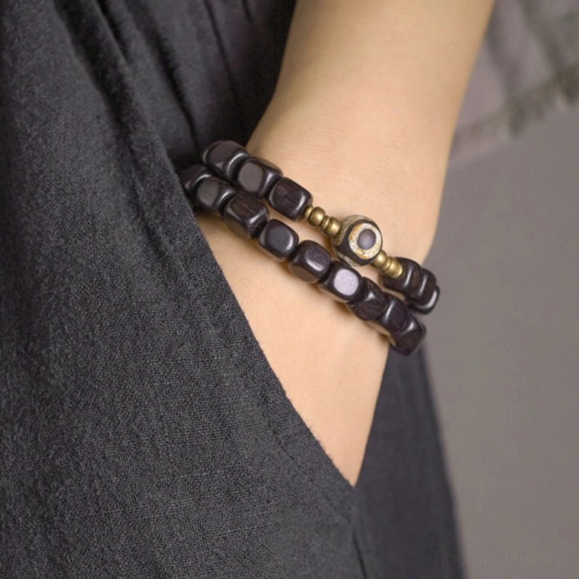 Side angle close-up of ebony wood dzi bead couple bracelet set on wrist with double-strand wooden beads and copper eye accent against dark fabric
