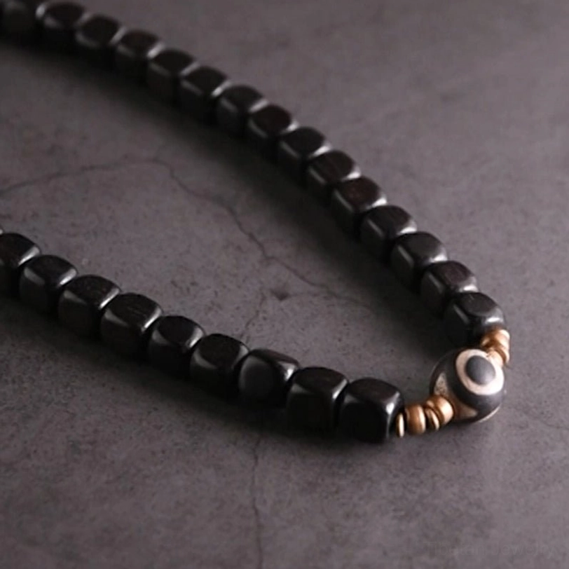 Close-up detail of ebony wood dzi bead couple bracelet showing black bead texture, hand-painted nine-eye charm, and copper connector elements