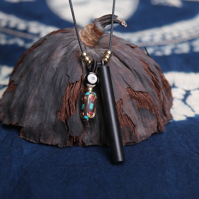 Close-up of ebony wood pendant with decorative dzi bead charm on indigo blue fabric background