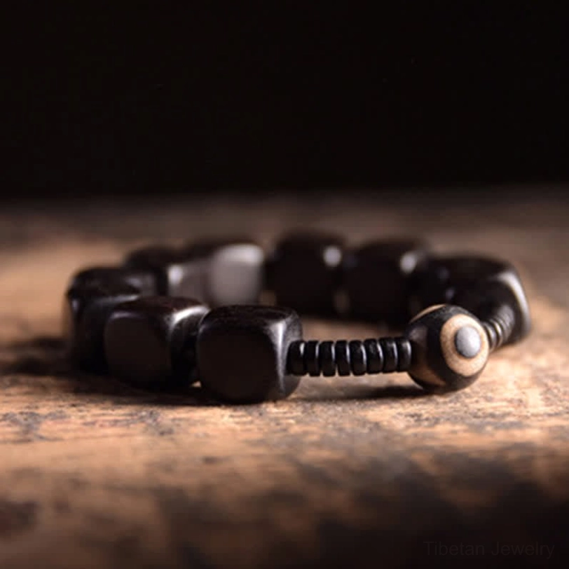 Handcrafted ebony wood dzi bracelet flat lay featuring polished black square beads round eye-patterned dzi accent and spiral spacers