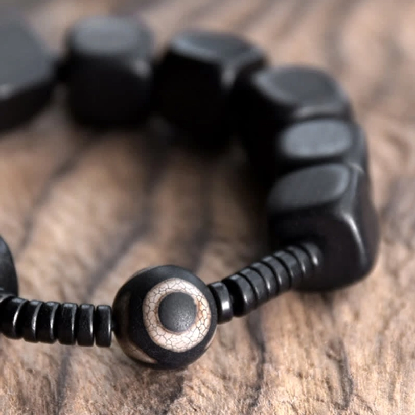 Ebony wood dzi bracelet detail shot showing two-tone round dzi bead with eye pattern spiral spacers and smooth square wooden beads