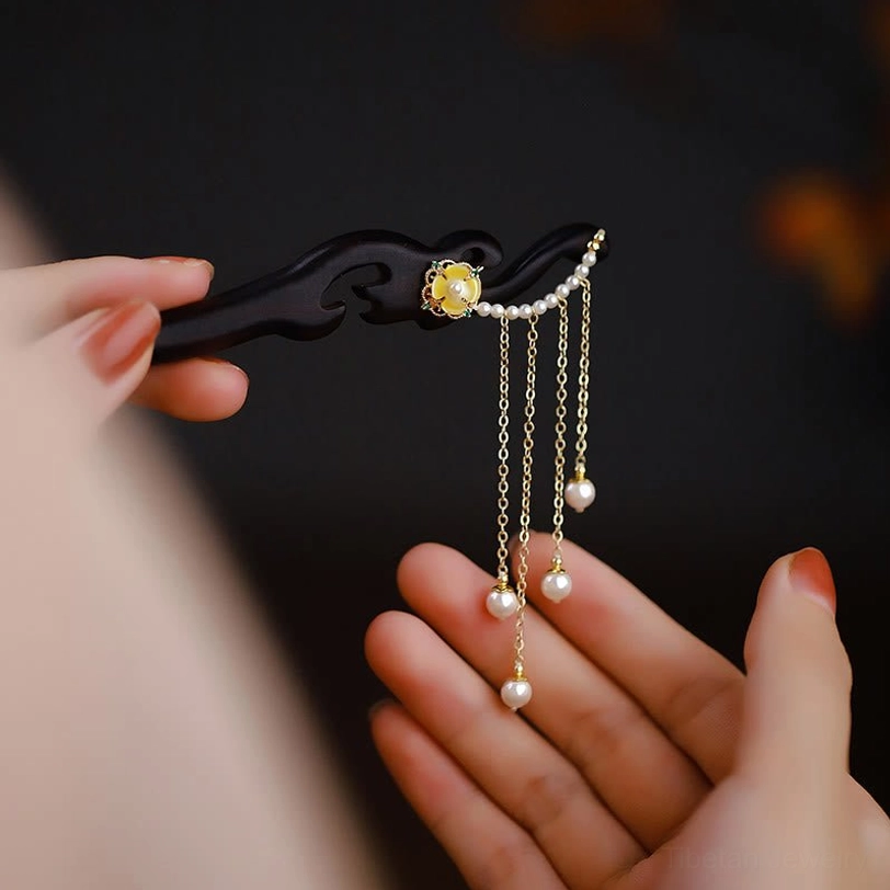 Front close-up view of ebony wood hairpin showing pearl tassel chains and yellow flower carved details