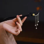 Ebony wood hairpin with yellow flower pearl tassels, side hand-held view showing carved details and copper-plated gold accents