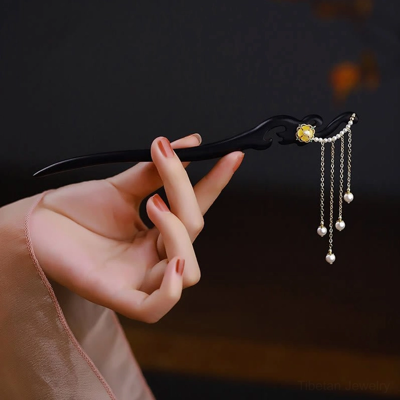 Ebony wood hairpin with yellow flower pearl tassels, side hand-held view showing carved details and copper-plated gold accents