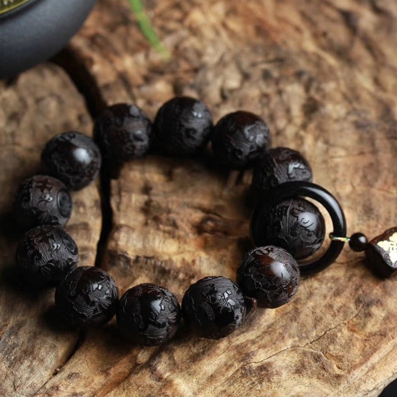 Ebony wood prayer bracelet with black ring accent and decorative charm, overhead shot on weathered wooden board