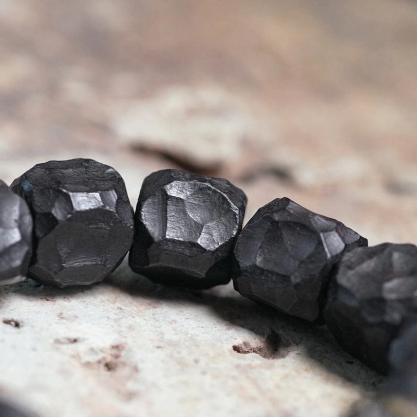 Close-up macro view of matte black faceted ebony wood beads and texture detail