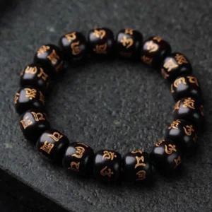 Close-up flat lay of authentic Tibetan mantra bracelet showing detailed golden engraved Sanskrit characters on matte black ebony beads