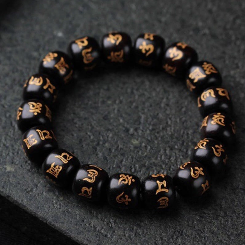 Close-up flat lay of authentic Tibetan mantra bracelet showing detailed golden engraved Sanskrit characters on matte black ebony beads