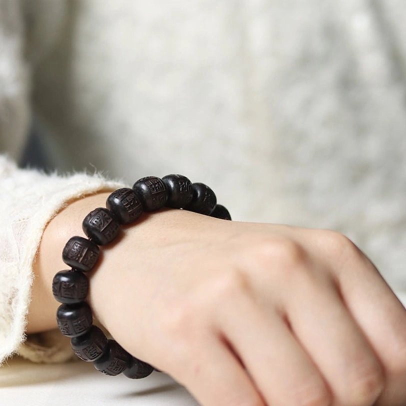 Tibetan wooden prayer bracelet on wrist displaying engraved sacred syllables in detail