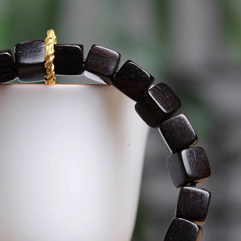 Close-up detail of ebony wood square beads showing natural grain texture and copper metal clasp
