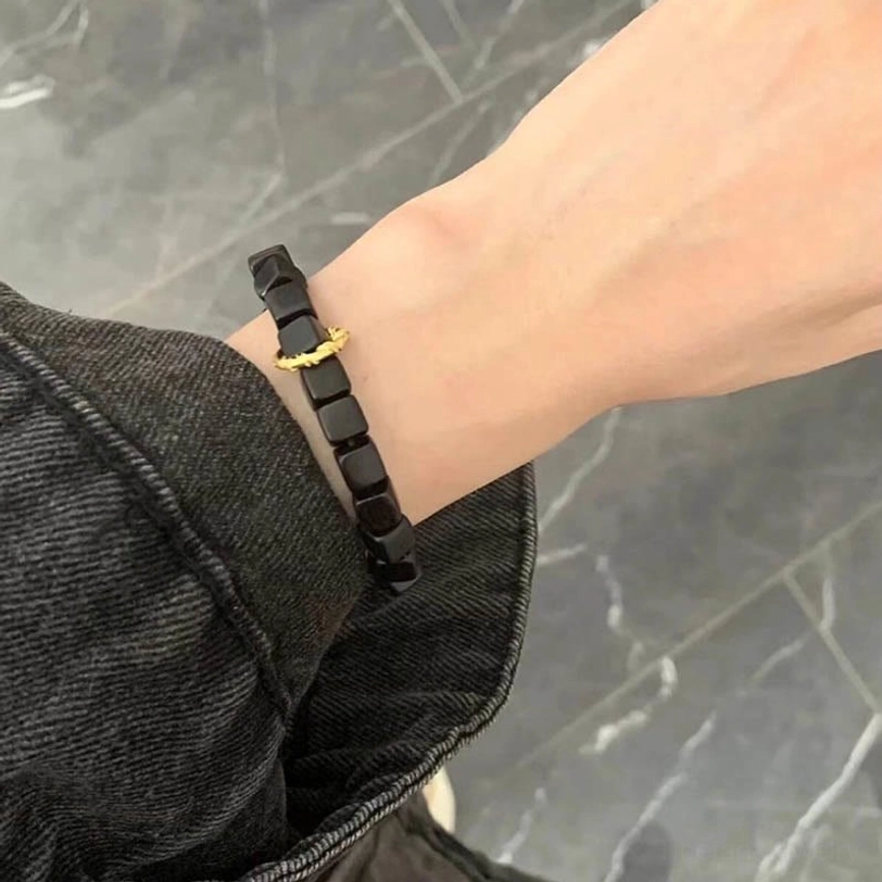 Ebony wood square bead bracelet with twisted copper decorative clasp worn on wrist against marble background
