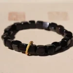 Ebony wood square bead bracelet with twisted copper clasp on light brown background with Chinese seal stamps