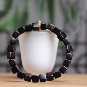 Handmade ebony wood square beads bracelet worn on wrist with elastic string design next to white ceramic mug