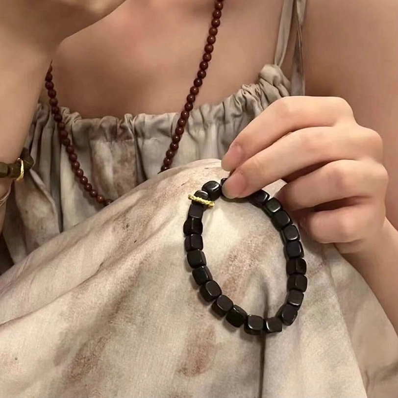 Ebony wood square bead bracelet held in hand paired with long wooden bead necklaces