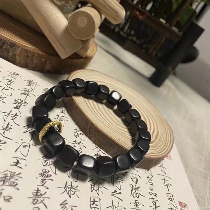 Two styles of ebony wood square bead bracelets with and without copper clasp on calligraphy paper