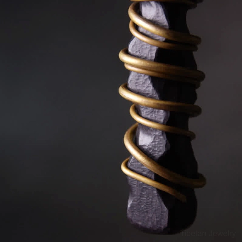 Macro view of brass wire wrapping on ebony wood Tibetan pendant, showcasing hand-coiled metalwork and wood texture