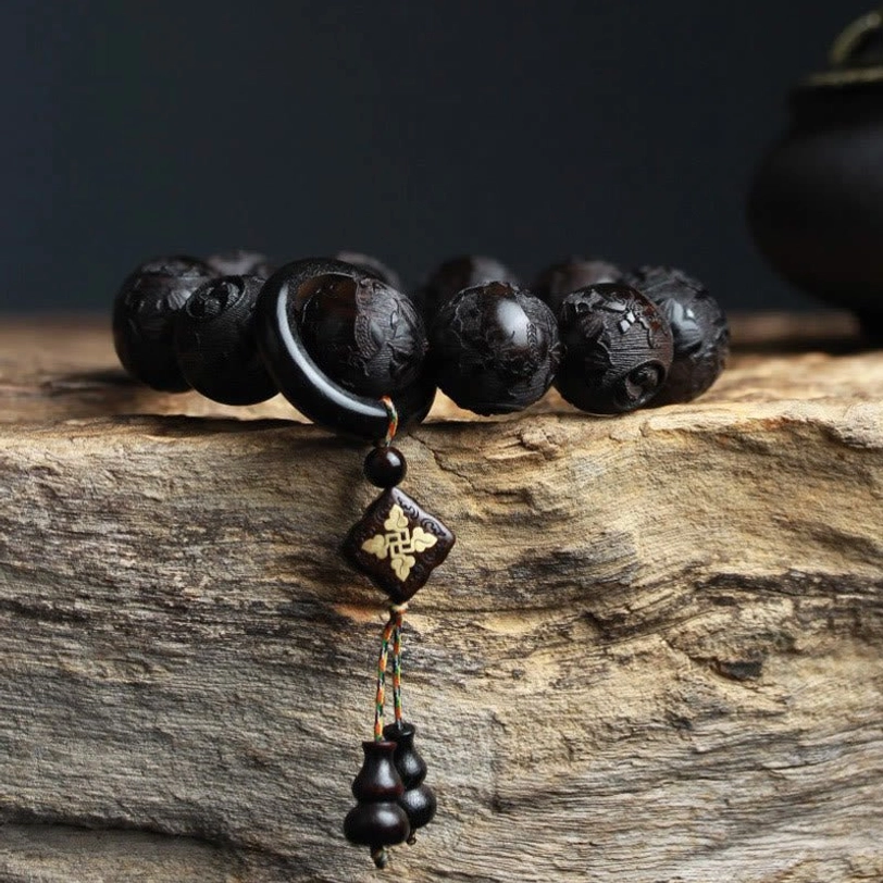 Side view close-up of ebony wood yin yang bracelet showing diamond-shaped charm with gourd tassel and carved bead details