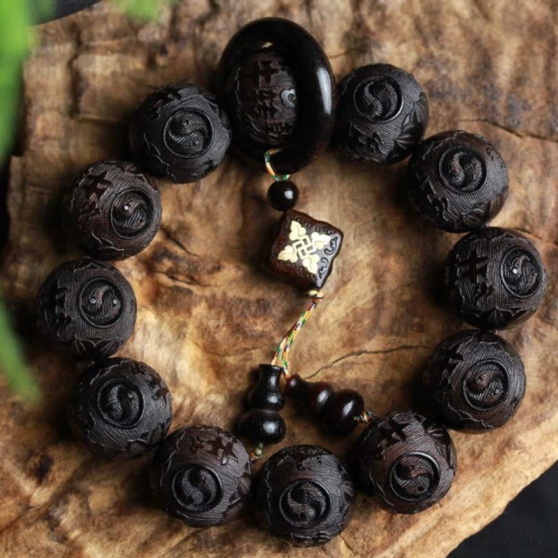 Ebony wood yin yang gourd bracelet with twelve hand-carved beads and decorative tassel charm, overhead view on rustic wood surface
